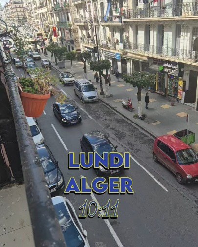 Une rue d'Alger bordée de grands immeubles blancs à balcons, vue depuis un balcon