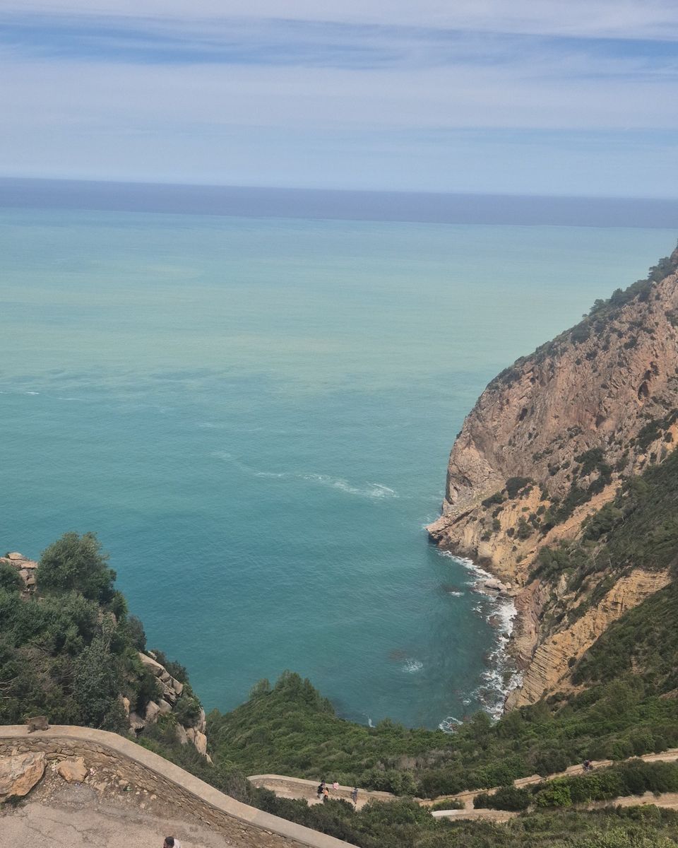 Des falaises couvertes de verdure plongent dans une mer turquoise, vues depuis un belvédère sur les hauteurs de Béjaïa