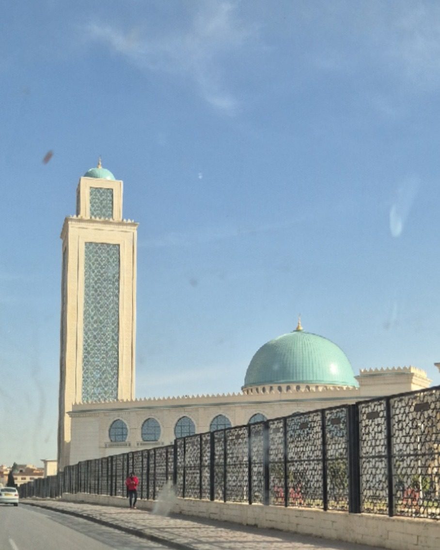 Une mosquée d'Oran avec son haut minaret et sa coupole verte, vue depuis la route