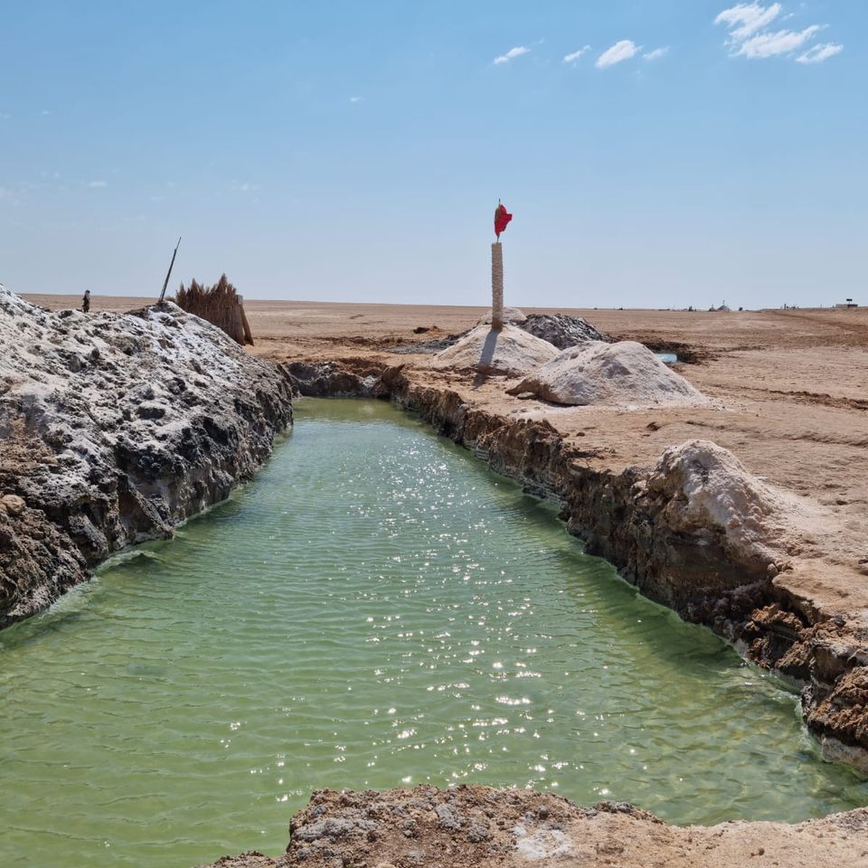 Un canal d'eau verte bordé de croûtes de sel, dans un paysage plat et désertique