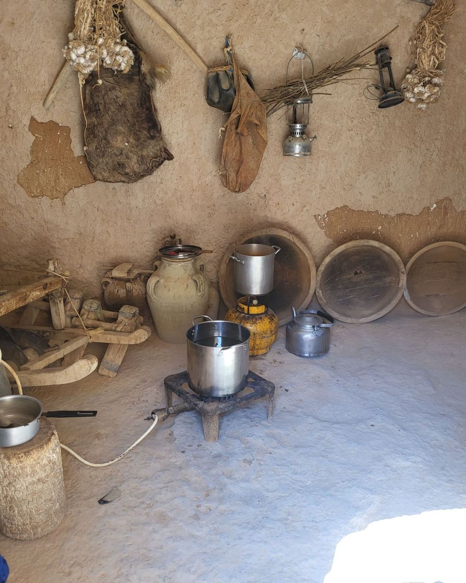La cuisine d'une maison troglodyte : jarres, marmites, lampes à pétrole et têtes d'ail suspendues au mur de terre