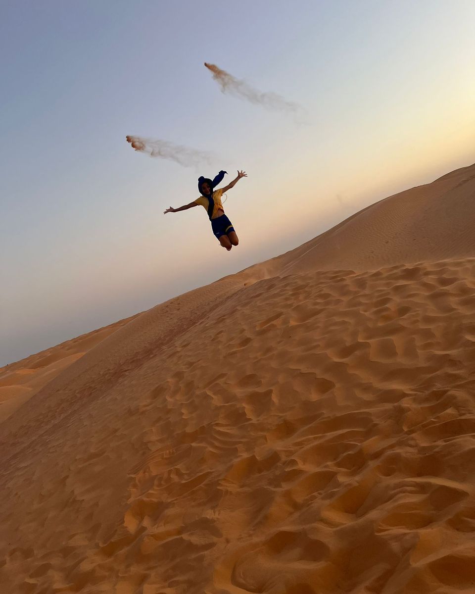 Une silhouette saute en l'air au sommet d'une dune de sable, au coucher du soleil
